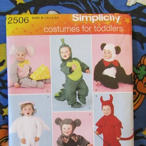 May include: Simplicity sewing pattern number 2506 for toddlers. The pattern includes five costumes: an elephant, a dragon, a panda, an angel, and a devil. The pattern is on a white background with a pink and orange border.