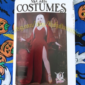 May include: McCall's Costumes sewing pattern for a vampire costume. The pattern features a white-haired woman wearing a red gown with a thigh-high slit and a long, flowing cape. The pattern is for sizes E5 (14-16-18-20-22).