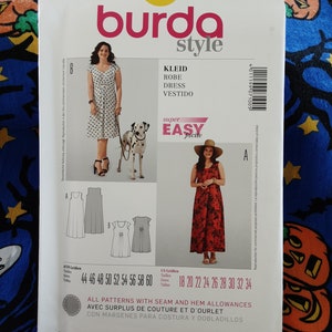 May include: A Burda Style sewing pattern packet, featuring dress designs. The packet includes images of the finished dresses, size charts, and the words "KLEID, ROBE, DRESS, VESTIDO" in a white background. The packet is white with a blue and orange background.