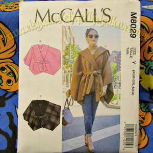May include: McCall's sewing pattern M8029 featuring a hooded cape with a tie closure. The pattern includes illustrations of the cape in pink and plaid fabric. The size is Y (XSM-SML-MED).