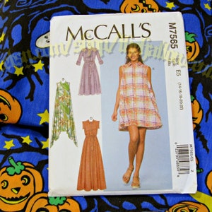 May include: A McCall's sewing pattern, M7565, with illustrations of four dress designs. The pattern is size E5, for sizes 14-22. The cover shows a woman in a plaid dress. The background is a blue fabric with Halloween-themed designs.