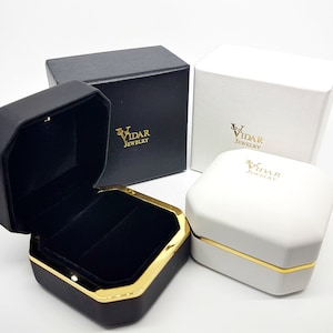 Puede incluir: Cajas de joyer&iacute;a octogonales negras y blancas con detalles dorados y el logotipo "VIDAR JEWELRY". Una caja est&aacute; abierta, revelando un interior de terciopelo negro. Las cajas son de varios tama&ntilde;os y formas, adecuadas para anillos u otras joyas peque&ntilde;as.