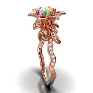Puede incluir: Anillo de oro rosa con un dise&ntilde;o floral y una piedra de &oacute;palo en el centro. La banda del anillo tiene un dise&ntilde;o ondulado con peque&ntilde;as piedras brillantes. Los p&eacute;talos de la flor y la banda est&aacute;n detallados, creando una joya elegante.