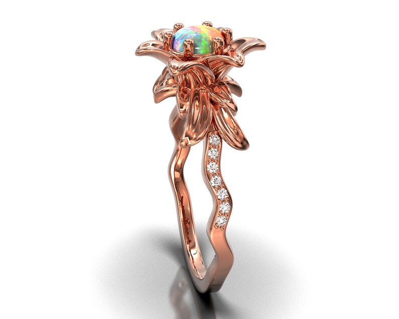 Puede incluir: Anillo de oro rosa con un dise&ntilde;o floral y una piedra de &oacute;palo en el centro. La banda del anillo tiene un dise&ntilde;o ondulado con peque&ntilde;as piedras brillantes. Los p&eacute;talos de la flor y la banda est&aacute;n detallados, creando una joya elegante.