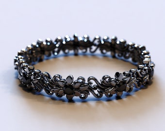 Op de afbeelding: Een zwarte metalen ring met een bloemmotief en zwarte edelstenen. De ring is delicaat en ingewikkeld.