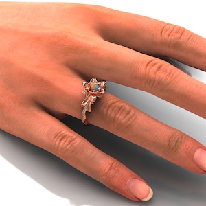 Puede incluir: Anillo de oro rosa con dise&ntilde;o floral y piedra central de &oacute;palo. El anillo presenta delicados detalles de hojas y vides con peque&ntilde;as piedras de acento. El anillo se muestra en una mano.
