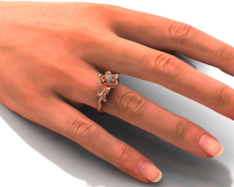 Puede incluir: Anillo de oro rosa con dise&ntilde;o floral y piedra central de &oacute;palo. El anillo presenta delicados detalles de hojas y vides con peque&ntilde;as piedras de acento. El anillo se muestra en una mano.