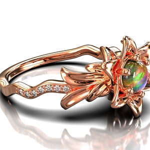 Puede incluir: Anillo de oro rosa con dise&ntilde;o floral y una piedra preciosa de &oacute;palo en el centro. La banda del anillo tiene un patr&oacute;n ondulado con peque&ntilde;as piedras preciosas transparentes. El &oacute;palo muestra colores verdes, azules y morados.