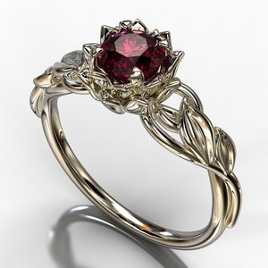 Peut inclure: Une bague en or avec une pierre précieuse rouge sertie dans un motif de fleur. La bande est ornée de détails délicats en forme de feuilles.