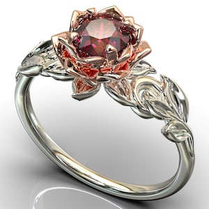 Puede incluir: Un anillo de plata y oro rosa con una piedra preciosa roja engastada en un diseño floral.