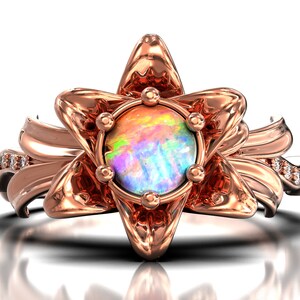 Puede incluir: Anillo de oro rosa con una &oacute;palo iridiscente en el centro, rodeado por un dise&ntilde;o floral estilizado. El anillo tiene peque&ntilde;os detalles de diamantes en la banda. El dise&ntilde;o es detallado y elegante, adecuado para ocasiones especiales.