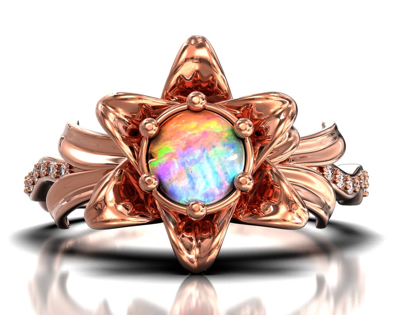 Puede incluir: Anillo de oro rosa con una &oacute;palo iridiscente en el centro, rodeado por un dise&ntilde;o floral estilizado. El anillo tiene peque&ntilde;os detalles de diamantes en la banda. El dise&ntilde;o es detallado y elegante, adecuado para ocasiones especiales.