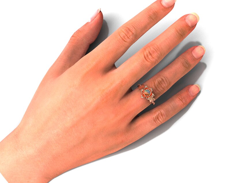 Puede incluir: Un anillo de oro rosa con una piedra preciosa de &oacute;palo, engastada en un dise&ntilde;o floral. El anillo est&aacute; en una mano sobre un fondo blanco. El &oacute;palo tiene una mezcla de colores, incluyendo blanco, naranja y azul.