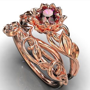 Può includere: Un anello di fidanzamento in oro rosa con un delicato design floreale. La pietra centrale è una pietra rotonda rosa circondata da pietre più piccole. La fascia è decorata con foglie e viti.