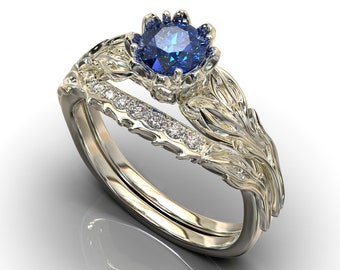 Puede incluir: Un delicado anillo de oro engastado con una gran piedra preciosa azul rodeada de pequeños diamantes. El anillo presenta un diseño floral con intrincados detalles.