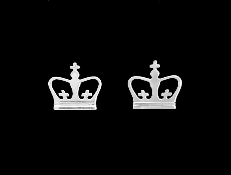 May include: A pair of silver crown-shaped earrings. The crowns have a simple design with a cross at the top and two smaller crosses on the sides.