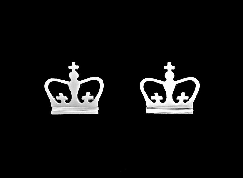 May include: A pair of silver crown-shaped earrings. The crowns have a simple design with a pointed top and three small circles on the crown.