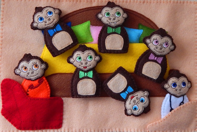 May include: A felt finger puppet play set featuring Seven brown monkeys with different colored bow ties. The monkeys are sitting on a yellow bed with brown and pink pillows. The set is perfect for imaginative play and storytelling.