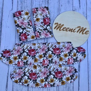 May include: A set of three floral print fabric pieces, including two rectangular pieces and one larger piece shaped like a bib. The fabric features a white background with pink, yellow, and green floral designs. The larger piece has the text "Meeni Me" printed on it.