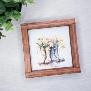 Może przedstawiać: Biały ceramiczny kubek z czarnym uchwytem i napisem "But First, Coffee" pogrubioną czcionką. Kubek jest ustawiony na rozmytym tle. Kubek ma około 10 cm wysokości.