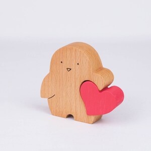 Peut inclure: Une figurine d'oiseau en bois tenant un cœur rouge. L'oiseau a un visage simple dessiné à la main.
