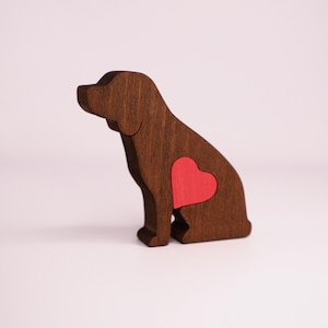 May include: A wooden dog figurine with a red heart cutout in its chest. The dog is sitting with its head turned to the side.