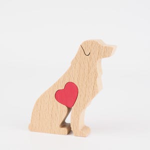 May include: A wooden dog figurine in a sitting position, featuring a red heart-shaped inlay on its side. The dog is made of light-colored wood with visible grain, and a black line defines the eye. The background is plain white.