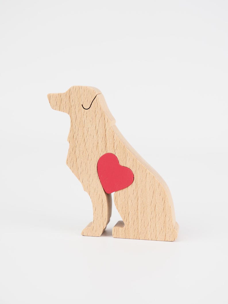 May include: Wooden dog figurine with a red heart-shaped insert. The dog is light brown with a simple black line for the eye. The figurine is sitting upright, with its tail tucked in.