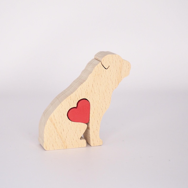Puede incluir: Figurita de perro de madera con un coraz&oacute;n rojo recortado en el &aacute;rea del pecho. El perro est&aacute; sentado con la cabeza girada hacia la derecha.