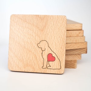 May include: A set of wooden coasters with a laser-cut design of a dog with a red heart on its chest. The coasters are stacked on top of each other.