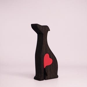 May include: A black wooden dog figurine with a red heart cutout in the back. The figurine is sitting on a white surface.