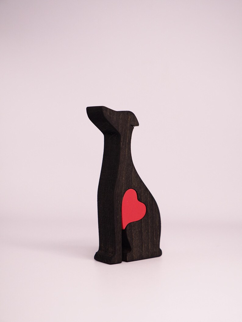 May include: A black wooden dog figurine with a red heart cutout in the back. The figurine is sitting on a white surface.