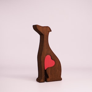 May include: A wooden figurine of a dog with a red heart cutout in its chest. The figurine is brown and has a simple, stylized design.