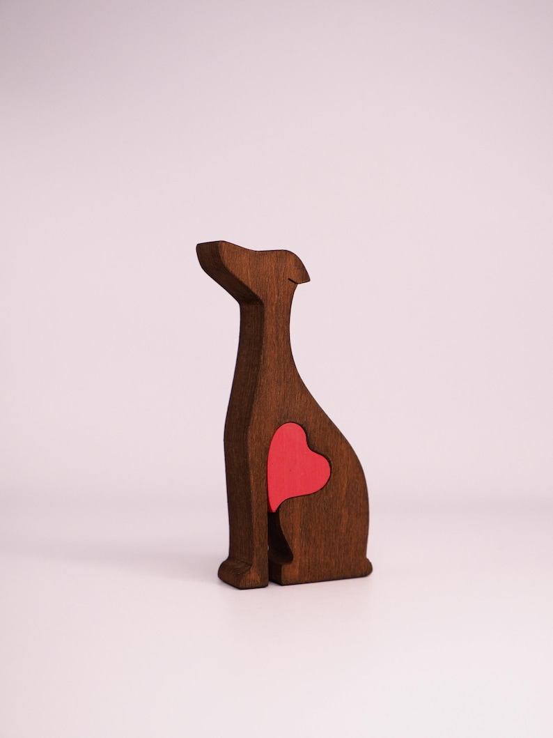 May include: A wooden figurine of a dog with a red heart cutout in its chest. The figurine is brown and has a simple, stylized design.