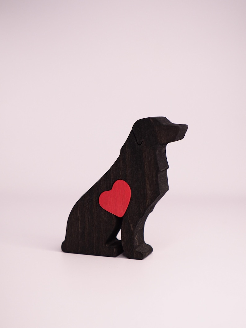 May include: A black wooden dog figurine with a red heart-shaped accent on its side. The dog is in a sitting position, with a smooth, polished finish. The background is a plain white.