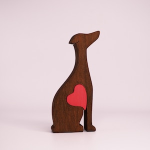 May include: A wooden cutout of a dog sitting with a red heart in its chest. The dog is brown and the heart is a bright red.
