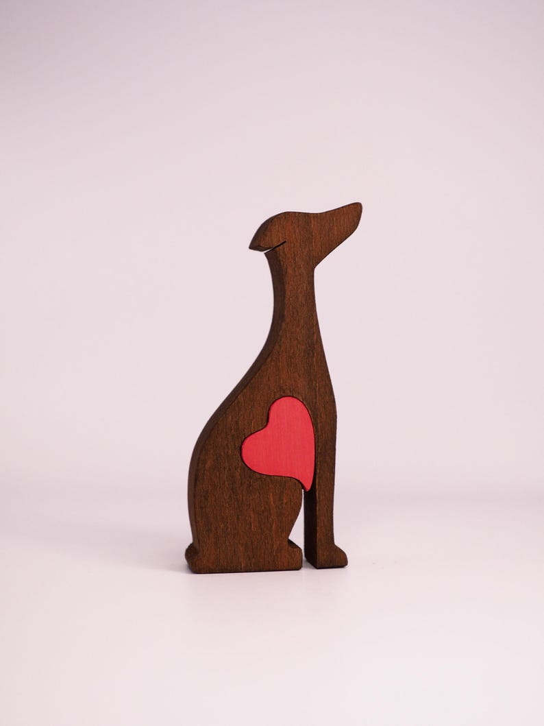 May include: A wooden cutout of a dog sitting with a red heart in its chest. The dog is brown and the heart is a bright red.