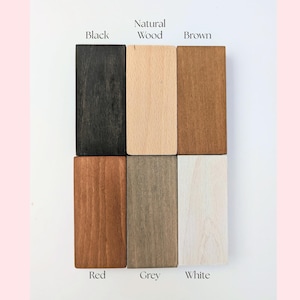 May include: A color palette of six rectangular wooden blocks, each displaying a different stain. The colors include black, natural wood, brown, red, grey, and white. The names of the colors are labeled above or below each block.