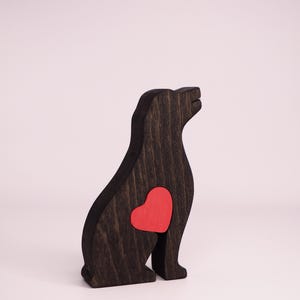 May include: A wooden dog figurine with a red heart cutout on its chest. The figurine is painted black and is sitting on a white surface.