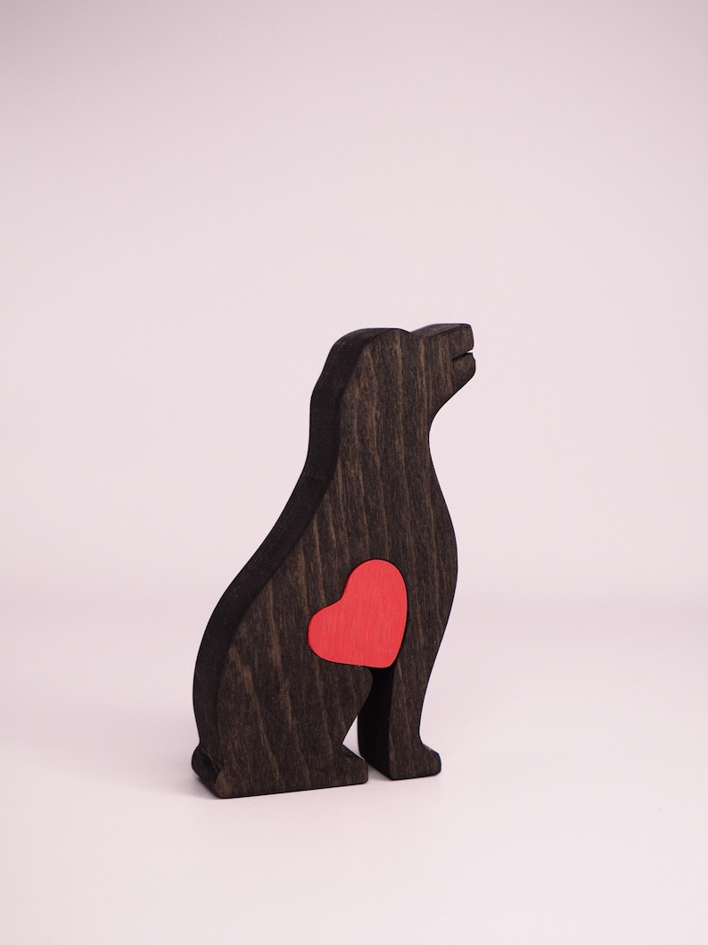 May include: A wooden dog figurine with a red heart cutout on its chest. The figurine is painted black and is sitting on a white surface.