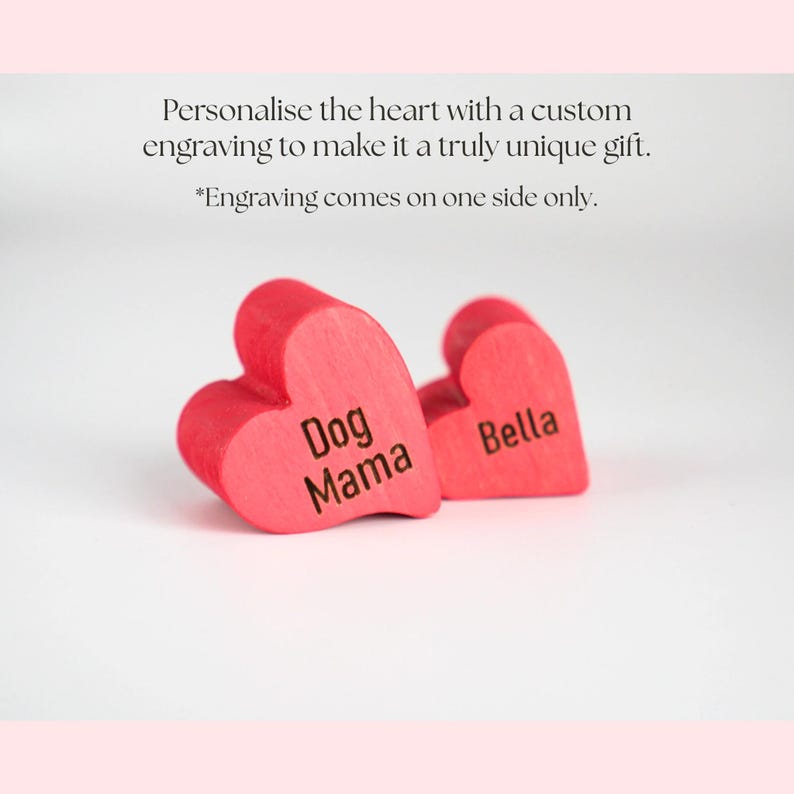 May include: Two red wooden heart-shaped ornaments. One heart is engraved with "Dog Mama", and the other with "Bella". The text above the hearts reads, "Personalise the heart with a custom engraving to make it a truly unique gift."