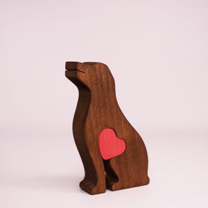 May include: A wooden dog figurine with a red heart cutout in its chest. The figurine is brown and has a simple, stylized design.