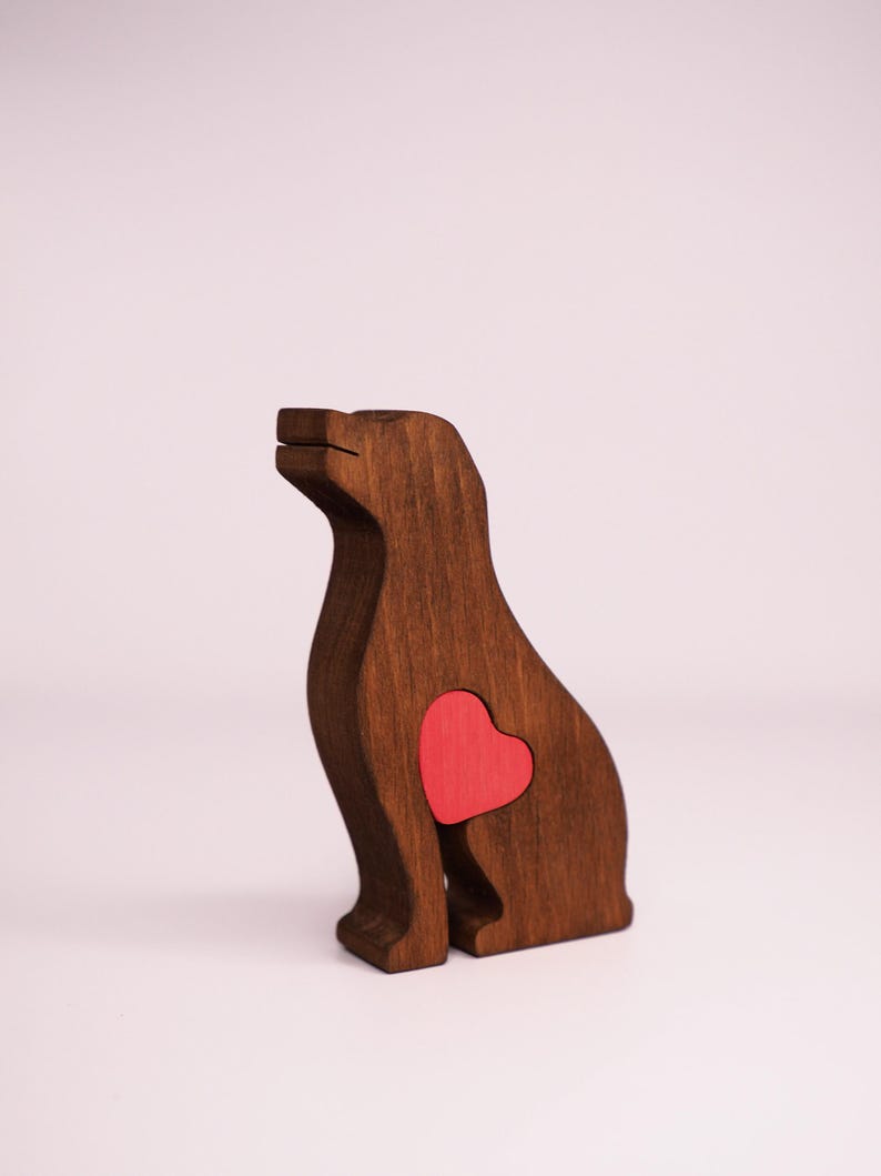 May include: A wooden dog figurine with a red heart cutout in its chest. The figurine is brown and has a simple, stylized design.