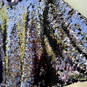 K&ouml;nnte beinhalten: Ein schwarzes Pailletten-Sweatshirt mit Rundhalsausschnitt und langen &Auml;rmeln. Die Pailletten sind eine Mischung aus Schwarz und Silber und erzeugen einen schimmernden Effekt. Das Kleidungsst&uuml;ck h&auml;ngt an einem Holzb&uuml;gel.