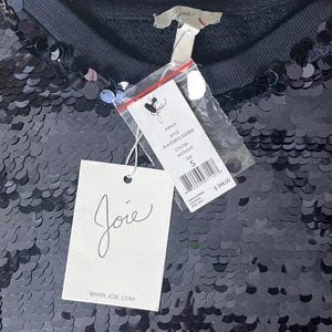 K&ouml;nnte beinhalten: Ein schwarzes Pailletten-Oberteil mit Rundhalsausschnitt und dem Markenetikett "Joie". Das Etikett lautet "Aldwyn", Farbe "Midnight" und Gr&ouml;&szlig;e "S". Das Oberteil ist mit kleinen, runden, reflektierenden Pailletten bedeckt.