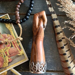 May include: A wooden sculpture of a clenched fist with a silver filigree base. The wood grain is visible, showcasing natural patterns. The sculpture is brown and has a smooth finish. The base is silver and has an ornate design.