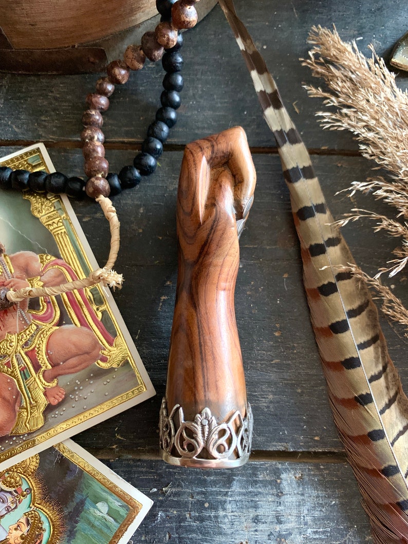 May include: A wooden sculpture of a clenched fist with a silver filigree base. The wood grain is visible, showcasing natural patterns. The sculpture is brown and has a smooth finish. The base is silver and has an ornate design.