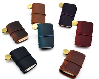 May include: Seven small leather-bound notebooks with elastic closures and brass accents. The notebooks are in various colors, including brown, black, red, purple, and teal.