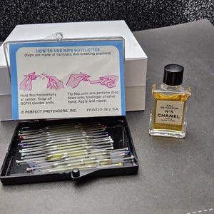 May include: A black tray filled with glass nip bottles, a small bottle of Chanel No. 5 perfume, and a white box. A blue and white card provides instructions on how to use the nip bottles.