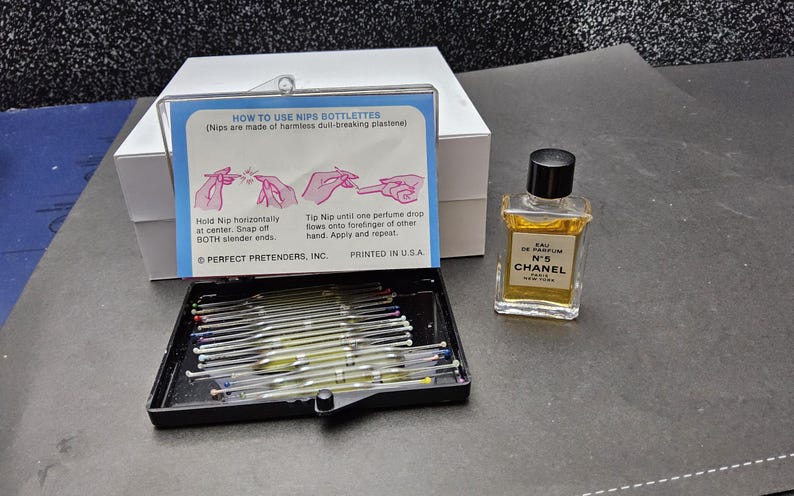 May include: A black tray filled with glass nip bottles, a small bottle of Chanel No. 5 perfume, and a white box. A blue and white card provides instructions on how to use the nip bottles.